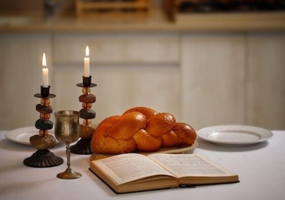 Traditioneller Challa-Zopf mit Kerzen, Kelch und aufgeschlagenem Buch