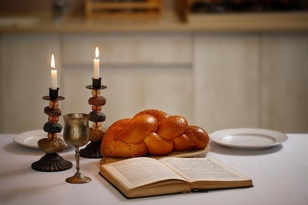 Traditioneller Challa-Zopf mit Kerzen, Kelch und aufgeschlagenem Buch